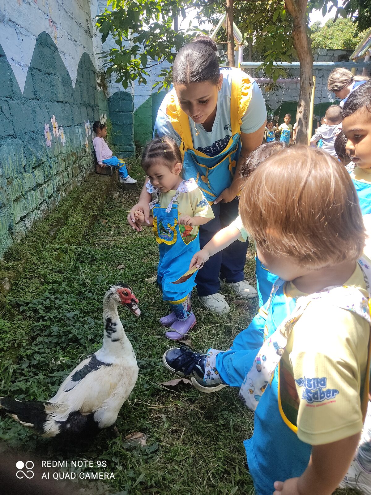 Docente y niños de overol azul junto a un pato sobre el césped