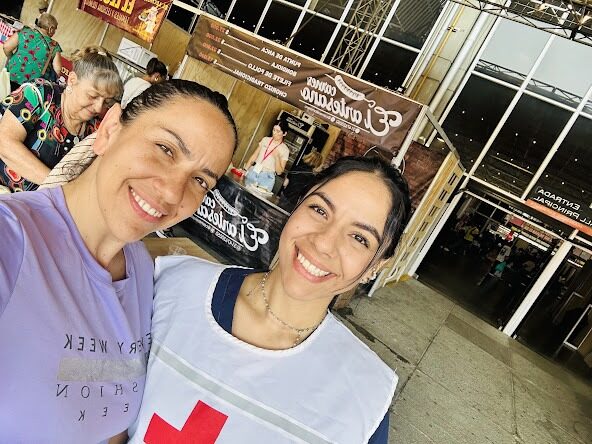 Selfie de dos mujeres sonrientes, una con uniforme lila y otra con peto blanco de la Cruz Roja, en la terraza de un local comercial