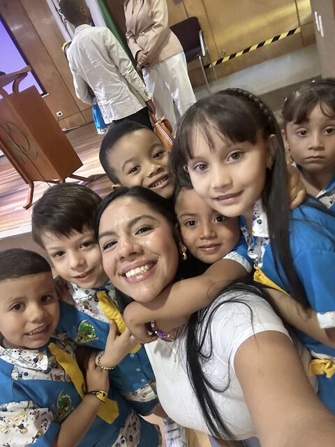 Docente sonriente tomándose una selfie rodeada de niños y niñas con uniforme azul y corbata amarilla