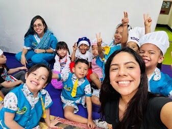 Selfie de una docente con un grupo de niños uniformados y otra docente al fondo, todos sonriendo en el aula