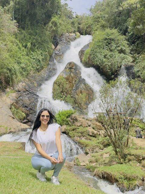 Mujer agachada frente a una cascada que baja entre rocas y vegetación
