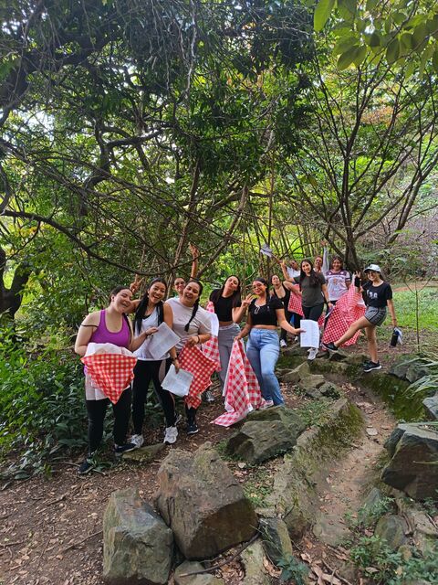 Grupo de mujeres posando al aire libre bajo grandes árboles, varias con manteles de cuadros rojos y blancos