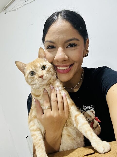 Joven sonriente de camiseta negra abrazando a un gato naranja