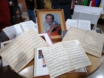 Partituras y cuadernos manuscritos del Maestro Elkin Pérez Álvarez dispuestos sobre una mesa alrededor de su retrato enmarcado