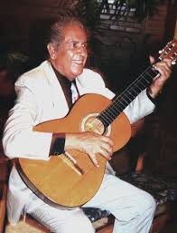 El Maestro Elkin Pérez Álvarez sonriente, vestido de blanco, tocando guitarra