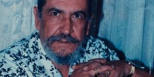 Primer plano del Maestro Elkin Pérez Álvarez con barba y bigote, camisa de flores y fondo azul